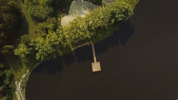 Vedere de sus a lacului cu dig de lemn pe fundalul pădurii. Clip. Frumos loc de țară pentru a vă relaxa în pădure verde cu lac. Casă de vacanță la țară cu lac și dig în vară — Fotografie, imagine de stoc