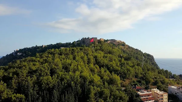 Vista superior de la fortaleza del casco antiguo en la montaña en el fondo del mar. Clip. Panorama de montañas verdes con fortaleza y bandera turca en el fondo del mar — Foto de Stock