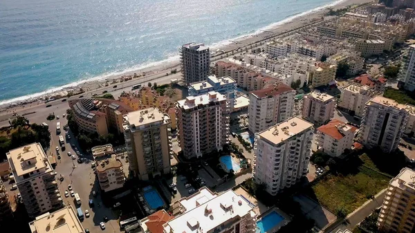 Vista dall'alto della bellissima grande città via mare sullo sfondo delle montagne. Clip. Panorama della località turistica meridionale situato sulla costa del mare blu e paesaggio montano — Foto Stock