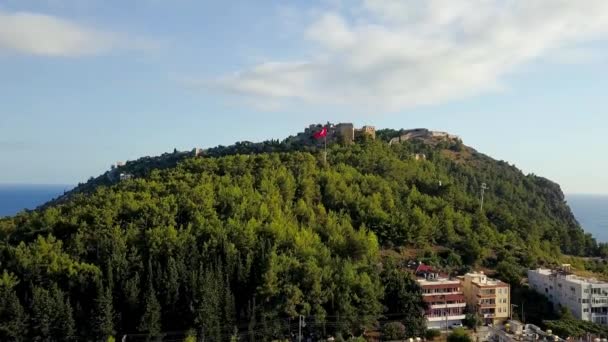 바다를 배경으로 산 위에 오래 된 도시의 요새가 보인다. 클립. 바다를 배경으로 요새 와 터키 국기가 있는 푸른 산들의 파노라마 — 비디오