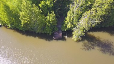 Barışçıl nehir ve orman kıyısı, insansız hava aracı tarafından vuruldu. Şarjör. Nehir, ahşap iskele ve güneşli bir yaz gününde kıyı boyunca uzanan birçok yeşil ağaçlı doğal manzara için hava..