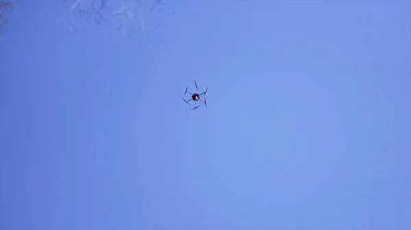 Vista inferior del dron con cuchillas giratorias volando en el cielo azul. Clip. Quadcopter con cuchillas giratorias que se elevan sobre el fondo claro del cielo brillante . —  Fotos de Stock