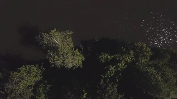 Zelená voda, dřevěné molo a zelené stromy, výhled z létajících dronů. Klip. Letecký pohled shora na nábřeží mezi stromy na břehu řeky v noci. — Stock fotografie