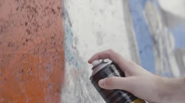 Hand hält eine Spraydose und zeichnet bunte Graffiti an die Wand, Street-Art-Konzept. Aktion. Seitenansicht eines Künstlers Gemälde mit Spray an der Wand, Betonmalerei. — Stockfoto