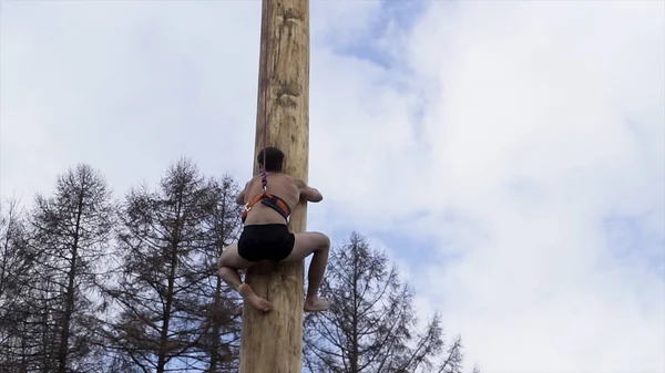 Mladík atletický stavět horolezectví na dřevěné kůlu o cenu, tradiční jarní karneval v Rusku. Akce. Dárky na tyči, ruský národní svátek Maslenitsa. — Stock fotografie