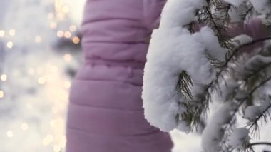Arka planda bulanık havai fişekler ve yılbaşı konseptiyle ağaç dalına yakın koşan bir kızın yan görüntüsü. - Sanat. Yeşil ladin dalından düşen kar ve maytap..
