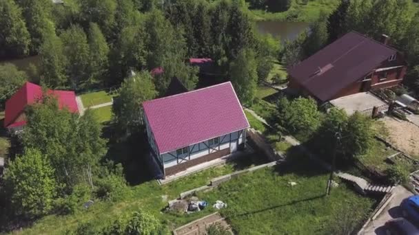 Vue aérienne du village de la rivière avec de belles maisons et de nombreux conifères verts, la vie dans le concept de la campagne. Clip. Nature estivale, maisons résidentielles au bord de la rivière . — Video