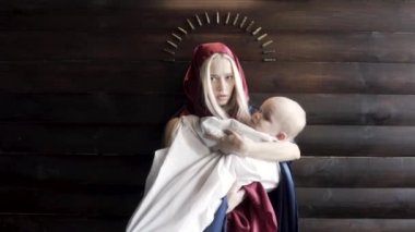 Kafası örtülü bir kadın, kollarında bebek olan bir anne kurşun, din ve savaş konseptiyle ahşap duvarın karşısında duruyor. Görüntü. Meryem Ana ve İsa 'nın görüntüsü..