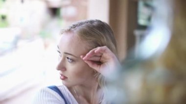 Kıvırcık saçlı genç ve güzel sarışın bir kadın dışarıda barda oturan ve başını elinin üzerine eğilmiş bir kenara bakarak. Madde. Bir yaz günü bar tezgahında Düşünceli kız.