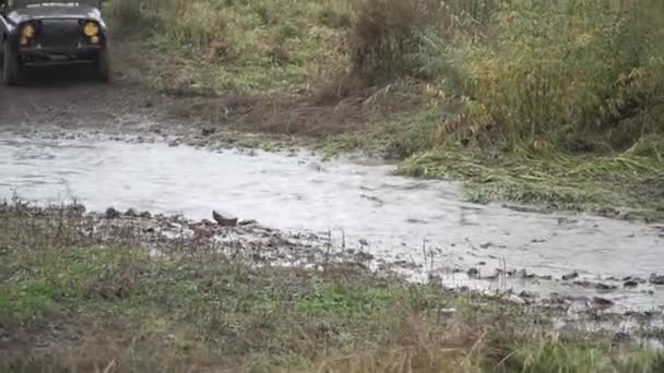 Una macchina sta guidando in campagna partecipando alla gara e attraversando ampie pozzanghere sporche, facendo schizzi d'acqua giganti, concetto di sport motoristici. Clip. Veicolo in pista, corsa fuoristrada . — Video Stock