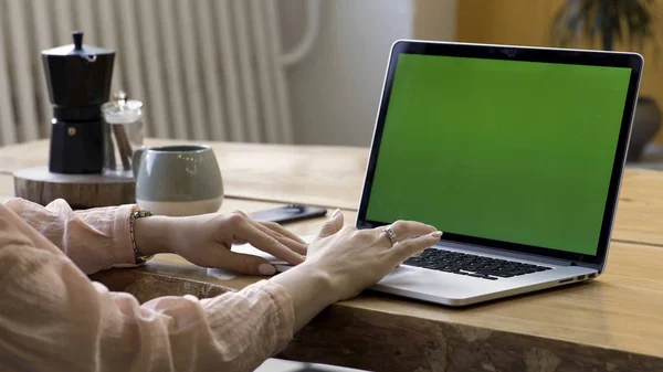 Close up para as mãos da mulher com um anel de ouro no dedo usando seu laptop com tela verde em pé na mesa no apartamento moderno. Imagens de stock. Local de trabalho em casa, laptop com chromakey . — Fotografia de Stock