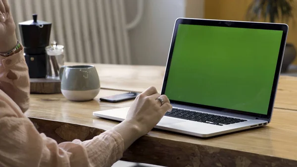 Close up para as mãos da mulher com um anel de ouro no dedo usando seu laptop com tela verde em pé na mesa no apartamento moderno. Imagens de stock. Local de trabalho em casa, laptop com chromakey . — Fotografia de Stock