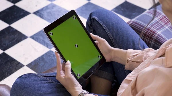 Manos de mujer usando tableta con pantalla verde, sentado en el sofá en casa, vista desde la parte posterior. Imágenes de archivo. Morena joven mujer mirando la tableta con croma key . — Foto de Stock