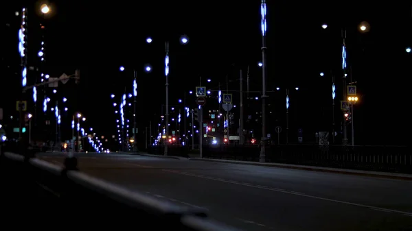 Hermosa vista nocturna de un camino urbano vacío con muchas luces a ambos lados de la carretera. Imágenes de archivo. Camino de la noche de verano iluminado por luz de neón de linternas . — Foto de Stock