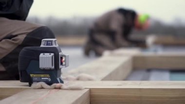 Ev temeli inşa ederken ahşap kiriş döşeyen özel korumalı üniformalı bir işçi. Şarjör. Ahşap bir çubuğun üzerinde duran bir lazer lazer aleti için kapat.