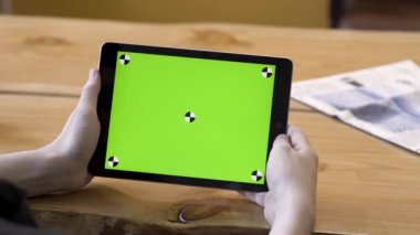 Tableti elinde tutan genç adam yeşil ekrana dokunuyor, üzerinde izleme işaretleri var, hareketsiz. Stok görüntüleri. Ahşap masa arka planında büyük kromakey monitörlü modern aygıt veya ipad.