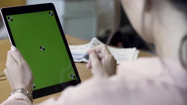 Vista sopra la spalla sulla donna nastratura e zoom su un dispositivo tablet con schermo verde mentre seduto al tavolo. Filmati delle scorte. vicino per le mani femminili utilizzando tablet, cromakey . — Video Stock