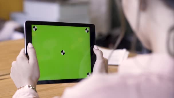 Achteraanzicht van een vrouw met een tablet met chromakey met volgsporen op houten tafelondergrond. Voorraadbeelden. Andere actie met het apparaat in daglicht binnenruimte, groen scherm. — Stockvideo