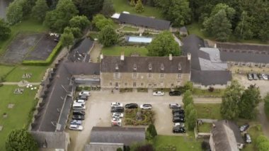 Modern yüzme havuzu ve park halindeki arabalarla tezat olarak yeşil ormanın yakınındaki taştan antik evin hava manzarası. Başla. Mimarlık konsepti, kırsal malikane.