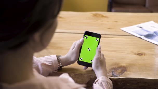 Gros plan de la fille assise à la table et utilisant un smartphone avec écran vert. Images d'archives. Vue sur l'épaule d'une femme sur l'appareil avec chromakey . — Video