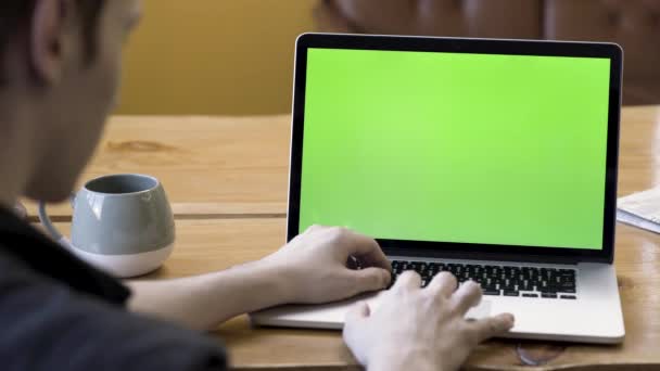 Вид сзади на мужские руки с помощью сенсорной панели рабочего ноутбука с хромакеем. Запись. Человек, работающий за компьютером с зеленым экраном, вид через плечо . — стоковое видео