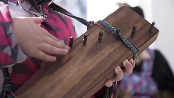 Close-up voor handen van een klein kind proberen ook het traditionele snaarinstrument te bespelen. Een knip. Een meisje dat buiten ongewone muziekinstrumenten bespeelt. — Stockvideo