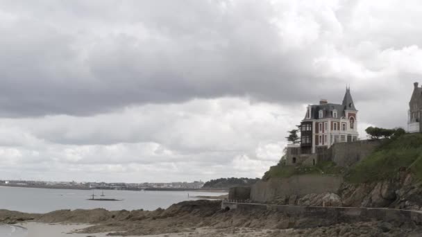 Panoramautsikt över stugorna med vita och röda tegelstenar på avsatsen vid havet. Börja. Sidovy över tegelhusen nära kusten linje på molnig himmel bakgrund. — Stockvideo