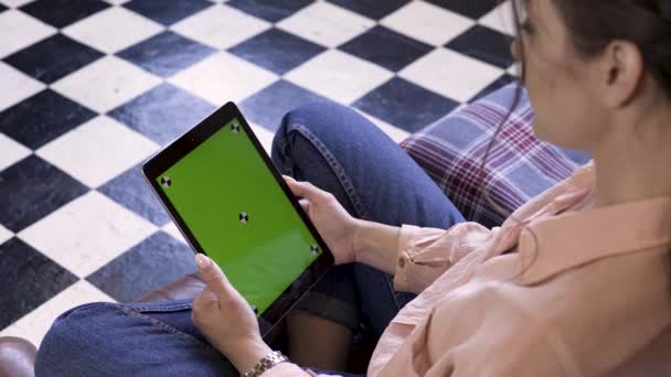 Mains de femme à l'aide d'une tablette avec écran vert, assis sur le canapé à la maison, vue du dos. Images d'archives. Brunette jeune femme regardant la tablette avec clé chromatique . — Video