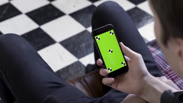 Masculino segurando telefone inteligente preto com tela verde e marcas de rastreamento no fundo do chão quadriculado preto e branco. Imagens de stock. Homem usando e assistindo no telefone celular com chave chroma . — Vídeo de Stock