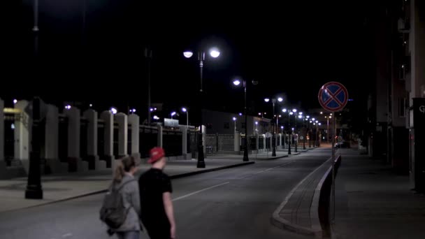 Couple walking across the empty urban street, night scenery in the city with street lamps on black sky background. Stock footage. Late evening road in modern residential area. — Stock Video