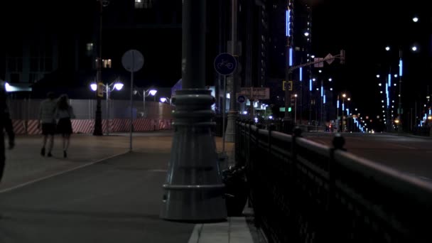 Люди идут по вечерней городской улице вдоль дороги, освещенной уличными фонарями на черном фоне неба. Запись. Ночной вид на улицу города с автомобилями и прохожими . — стоковое видео