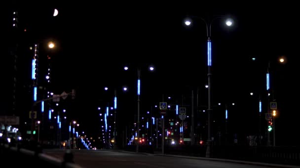 Nocny ruch miejski na ulicy z samotnym poruszającym się samochodem na tle czarnego nieba. Materiał filmowy. Piękna droga późnym wieczorem z lampami ulicznymi po obu stronach i jazda samochodem. — Wideo stockowe