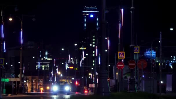 Arka planında gökdelen olan sokak lambaları boyunca giden arabaların olduğu bir gece şehrinin caddesi, Ekaterinburg, Rusya. Stok görüntüleri. Gece yolunda giden arabalar, zaman aşımı.. — Stok video