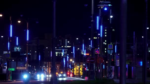 Calle de una ciudad nocturna con coches en movimiento a lo largo de farolas con un rascacielos en el fondo, Ekaterinburg, Rusia. Imágenes de archivo. Coches que conducen en el camino nocturno, lapso de tiempo . — Vídeo de stock