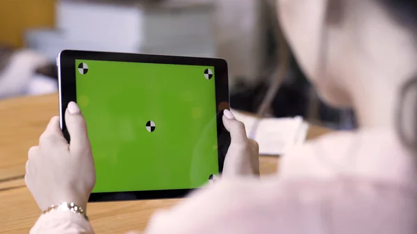 Visão traseira de uma mulher segurando um tablet com chromakey com marcas de rastreamento no fundo da mesa de madeira. Imagens de stock. Ação diferente com o dispositivo no espaço interno da luz do dia, tela verde . — Fotografia de Stock