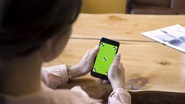 Primer plano de la niña sentada en la mesa y el uso de teléfono inteligente con pantalla verde. Imágenes de archivo. Vista sobre el hombro de una mujer en el dispositivo con chromakey . — Foto de Stock