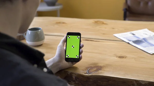 Vista sobre el hombro de un hombre de negocios utilizando el teléfono celular de mano con pantalla táctil verde sobre fondo de mesa de madera. Imágenes de archivo. Hombre lloking en su dispositivo, chromakey . — Foto de Stock