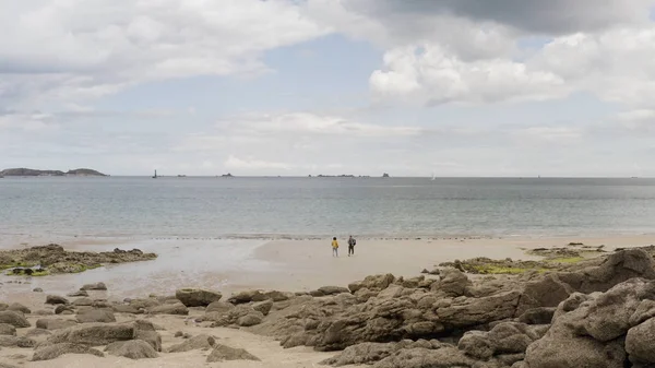 Par går på stranden med stenig strand med lugnt hav och blå molnig himmel på bakgrunden. Börja. Man och kvinna går på sandkusten. — Stockfoto