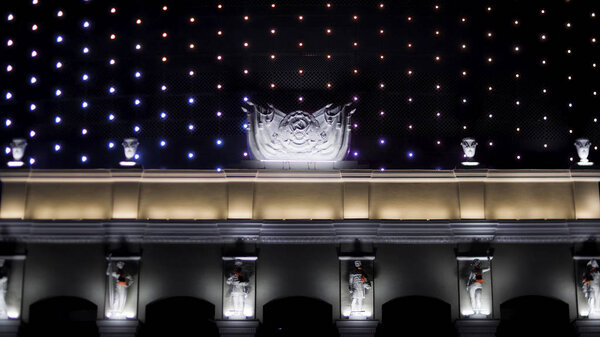 Bright illuminated facade of the soviet building at night with the Hammer and Sickle symbol. Stock footage. Beautiful house exterior decorated with flashing lights.