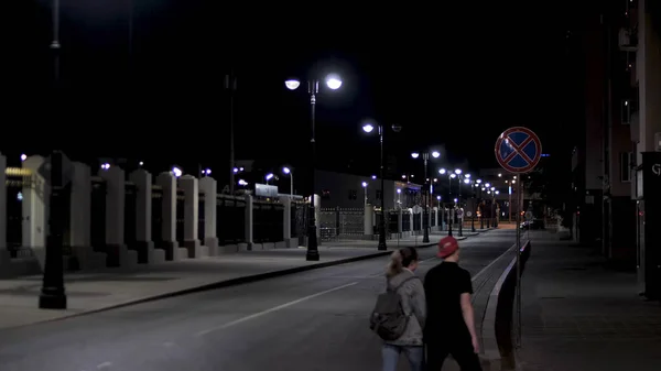 Couple walking across the empty urban street, night scenery in the city with street lamps on black sky background. Stock footage. Late evening road in modern residential area. — Stock Photo, Image