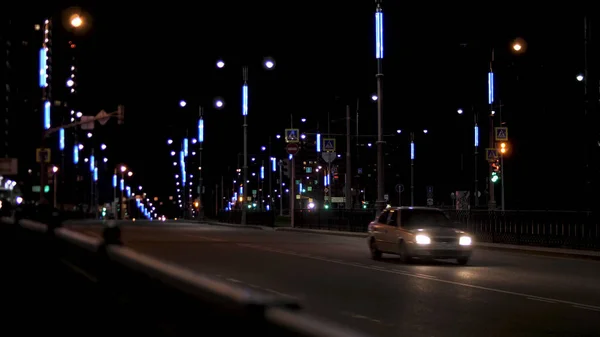 Natttrafiken på vägen, ensam bil som kör längs gatlyktorna. Lagerbilder. Night city väg med gatubelysning och flytta bil på mörk himmel bakgrund. — Stockfoto