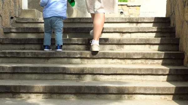 紧紧地抓住一个女人的手，帮助她的小孩爬上楼梯。 库存录像。 妈妈带着小孩的儿子走上楼梯. — 图库照片