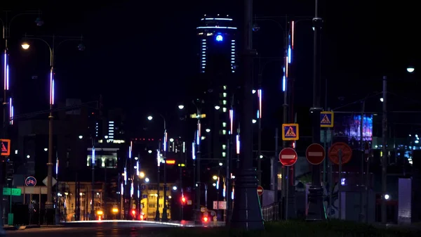 Night landscape of a modern city full of neon lights with cars moving on the road. Stock footage. Night road lit by many neon street lamps and driving cars.