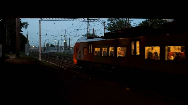 The train passing under the bridge in the summer evening, transportation concept. Stock footage. Train wagons with people inside running on the rails.