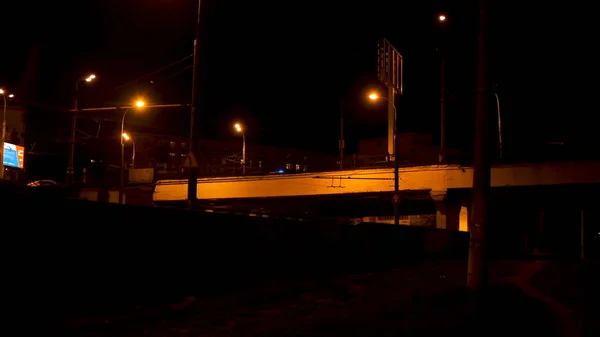 Nachtbrücke beleuchtet von Straßenlaternen mit fahrenden Autos auf schwarzem Himmelhintergrund. Archivmaterial. Stadtbrücke im Licht der Straßenlaternen mit fahrenden Fahrzeugen. — Stockfoto