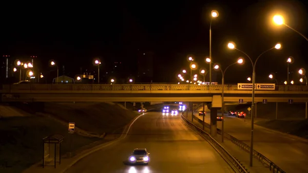 Aéreo para a rua noturna com carros de condução no fundo do céu preto. Imagens de stock. Tráfego noturno, estrada larga, a ponte iluminada por muitas luzes de rua e veículos em movimento . — Fotografia de Stock