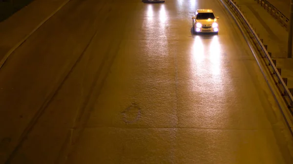 Vista aérea de la carretera de la ciudad por la noche iluminada por farolas con coches en movimiento, tráfico nocturno. Imágenes de archivo. Vista superior de los vehículos que conducen en el camino oscuro bajo las luces de la calle . — Foto de Stock