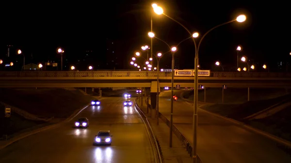 Cena bonita da rua à noite com muitos carros, tráfego noturno. Imagens de stock. Estrada noturna tardia sob as luzes de rua cheias de veículos dirigindo em direções diferentes . — Fotografia de Stock