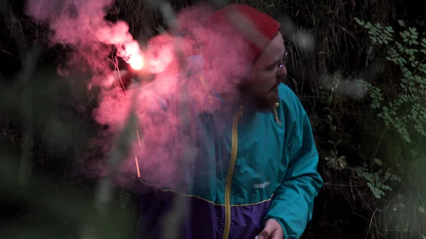 Hiker lost in the evening forest lighting a red signal flare and starting to wave his arm. Stock footage. Burning signal flare held by a worried man in the woods.