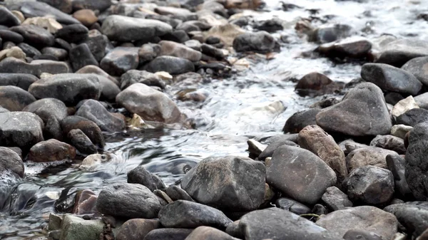 Close up of river stream flowing down over the grey stones. Stock footage. Fast and cold brook with clear water flowing on rocky area.